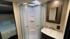 A bathroom with a shower, a sink, and a mirror. - Wildwood glamping rv - Site #72 (Klamath)