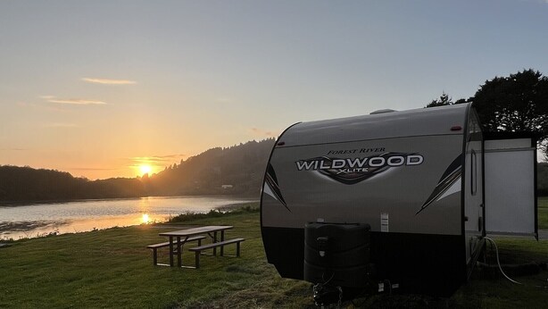 A Wildwood XLITE RV parked by a lakeside with a picnic table and a small shed nearby. - Wildwood glamping rv - Site #72 (Klamath)