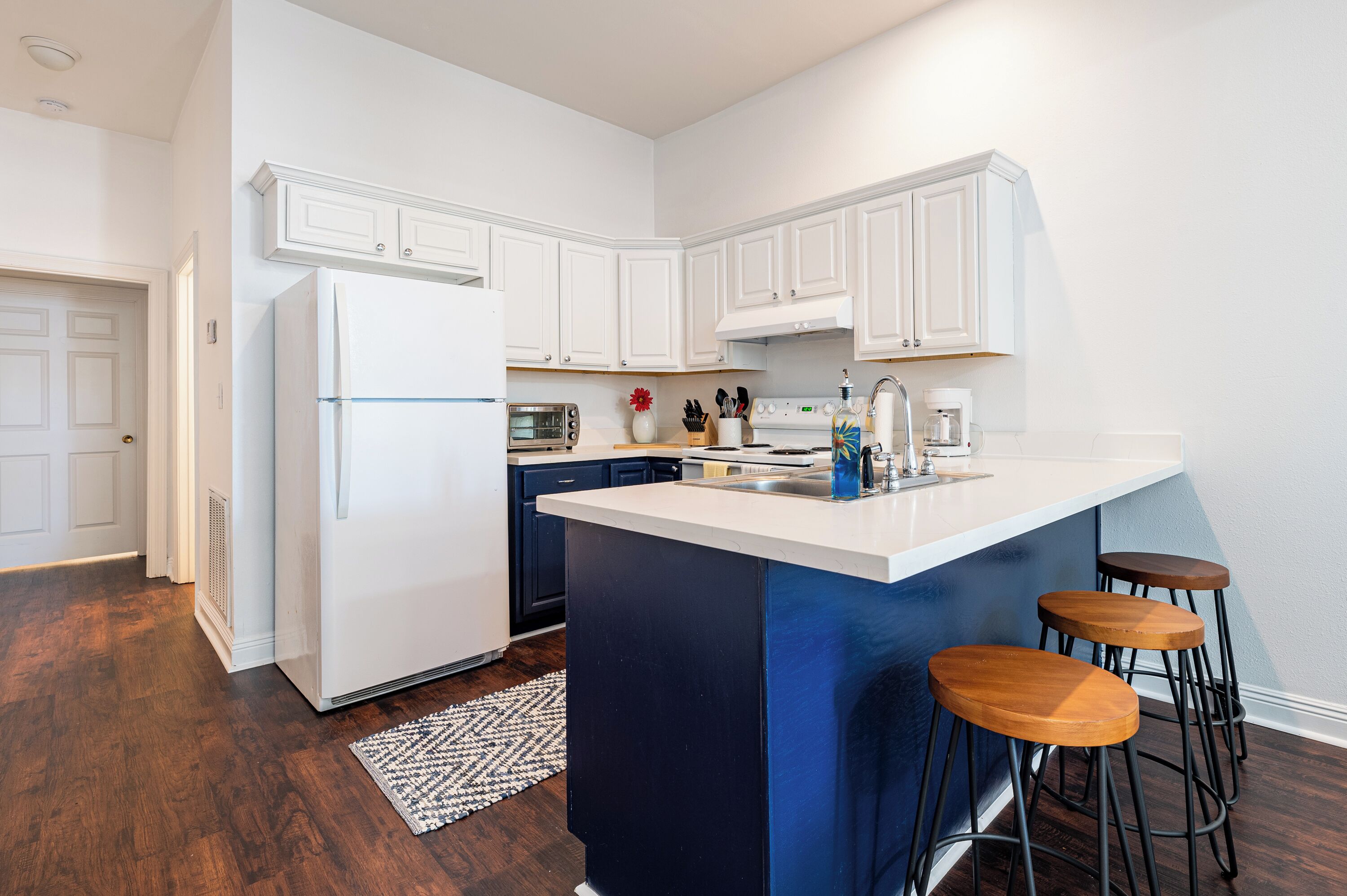 A modern kitchen with white cabinets, a central island with stools, a built-in oven, and a refrigerator.