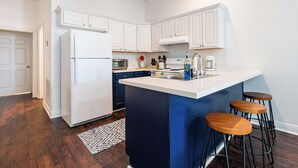 Una cocina moderna con armarios blancos, una isla central con taburetes, horno empotrado y refrigerador.