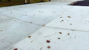 Een verharde oprit die leidt naar een gebouw, omringd door bomen.