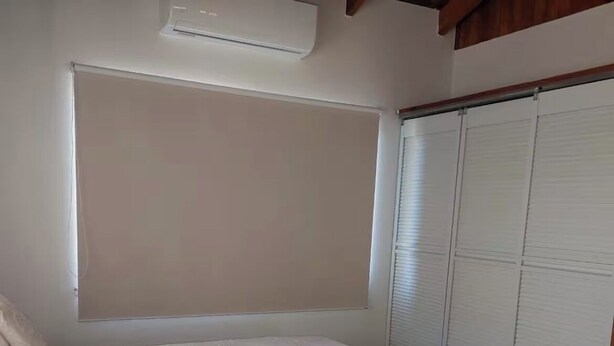 Un dormitorio con dos camas, una ventana con persiana y una puerta corrediza.