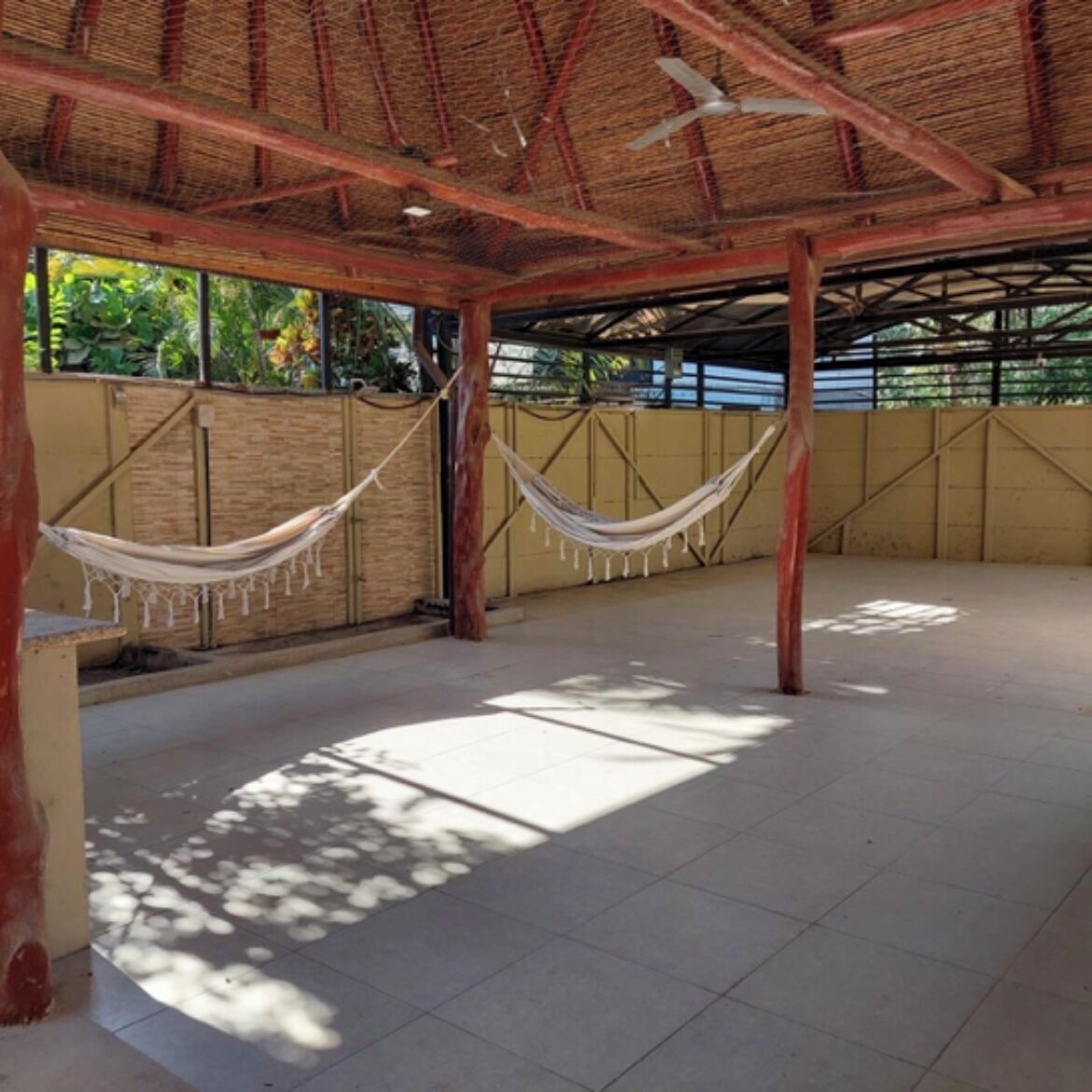 Eine überdachte Terrasse im Freien mit gefliestem Boden, zwei Hängematten und einem Deckenventilator.
