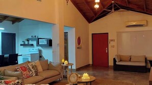 Amplia sala de estar con techo alto, una cocina al fondo y una puerta roja.