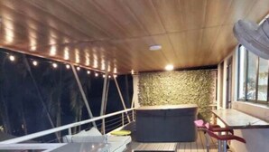 Un espacio al aire libre cubierto con piso de madera, muebles de mimbre e iluminación con luces colgantes.