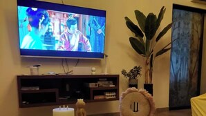Una sala de estar con un televisor montado en la pared, una mesa redonda con un objeto decorativo y una planta en maceta.