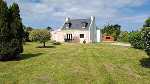A two-story house with a sloped roof, a front porch, and a small shed in the backyard. - Renovated, detached belle-illoise family home, 3 bedrooms, sleeps 9 (Le Palais)