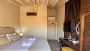 Una habitación de hotel con una cama grande, un escritorio de madera, un televisor y un pequeño otoman amarillo.