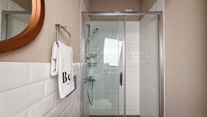 Un baño moderno con ducha envuelta en vidrio, paredes de azulejos blancos y un espejo grande con marco de madera.