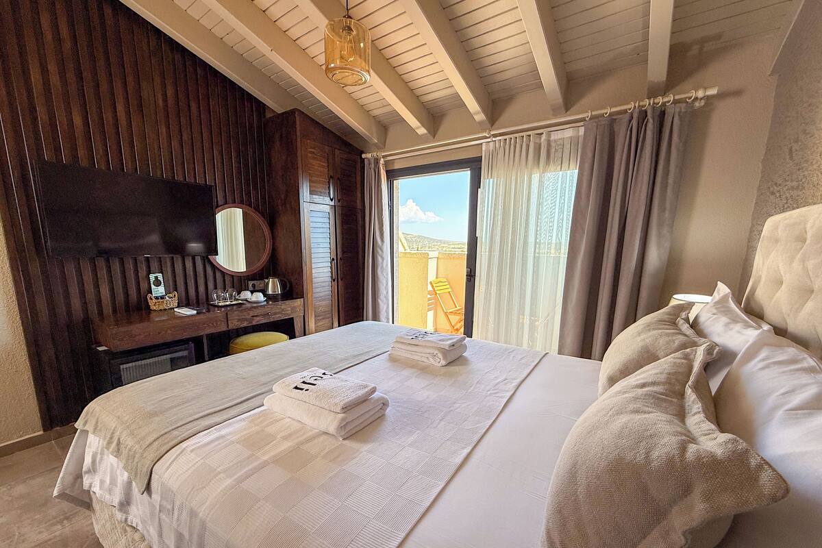 Habitación de hotel con una cama grande, un escritorio con silla, un espejo y vistas al exterior.