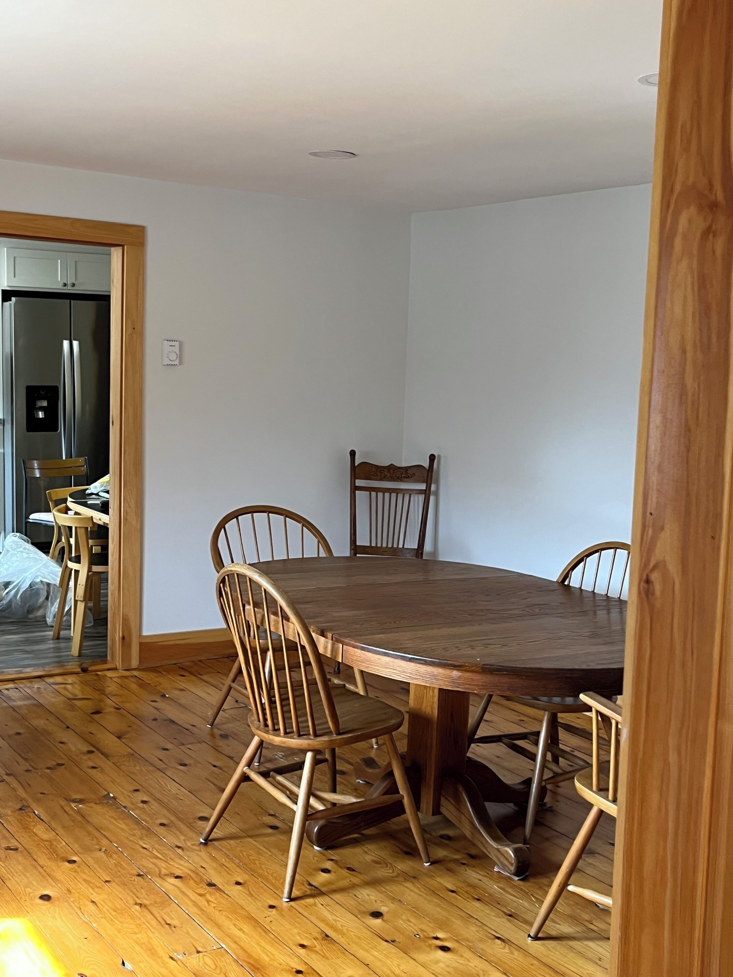 Een eetgedeelte met een houten tafel en vier stoelen, een houten vloer, en een keuken met een roestvrijstalen koelkast.