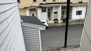 Una escalera de madera que lleva a un balcón con baranda blanca, con vistas a una calle con coches estacionados y edificios.