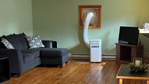 Una sala de estar con un sofá seccional, una mesa de centro de vidrio, piso de madera, un purificador de aire blanco y un televisor sobre un mueble de madera.