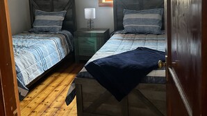 Un dormitorio con dos camas individuales, una mesita de noche con lámpara, una ventana y suelo de madera.