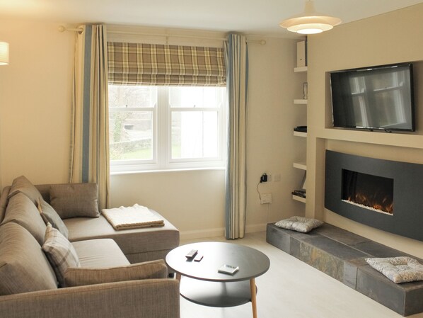A living room with a sofa, a round coffee table, a TV, and a fireplace. - 1 bedroom accommodation in Keswick (Keswick)