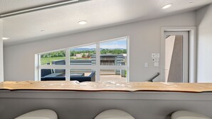 A modern room with a large window, a wooden table, and a view of a building complex. - Mountain View Getaway - Groups Welcome! (Fort Collins)