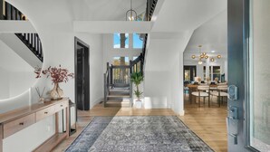 Un interior espacioso y moderno con piso de madera, un tapete grande, una escalera y un comedor con candelabro.