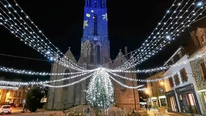 Ein historisches Gebäude mit einem markanten Turm, umgeben von Lichterketten und einem großen, beleuchteten Baum.