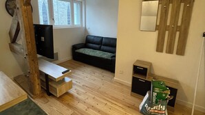 Ein Zimmer mit Schlafkoje, einer schwarzen Couch, einem kleinen Tisch und einem Fenster mit Blick auf eine Steinmauer.