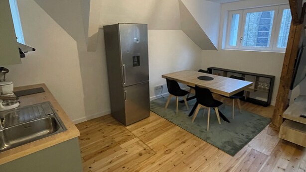 Eine kleine Küche mit eingebautem Kühlschrank, einem Holztisch mit Stühlen und einem Fenster.
