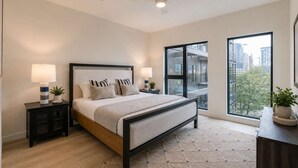 A modern bedroom with a large bed, two bedside tables with lamps, a view of the city through large windows, and a ceiling fan. - Loftline Social - 8BR | 6BA | Sleeps 20 (Nashville)