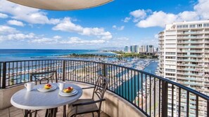 Ein Balkon mit Tisch und Stühlen mit Blick auf einen Yachthafen, Boote und einen Strand.
