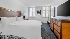 Ein Hotelzimmer mit einem großen Bett, einem Schminktisch, einem Fernseher und einem Fenster mit Jalousien.