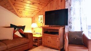 Ett mysigt vardagsrum med ett träpanelat tak, en platt-TV, en soffa, en fåtölj och ett soffbord.