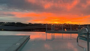 Una piscina con vista al atardecer, un área techada y una barandilla de metal.