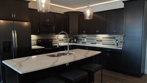 Una cocina moderna con armarios oscuros, una isla de mármol, electrodomésticos de acero inoxidable e iluminación colgante.