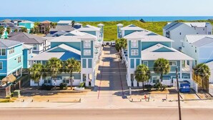 Un área residencial costera con varias casas de dos pisos, una vista despejada de la playa y una carretera que conduce a ella.