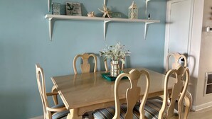 Un comedor con una mesa y sillas de madera, un jarrón con flores y estantes con diversos objetos decorativos.