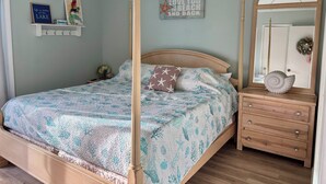 Un dormitorio con cama con dosel, cómoda con cajones, espejo y adornos en la pared, incluyendo una estrella de mar y un letrero.