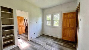 Una habitación con piso de madera, paredes blancas, una ventana y una puerta.