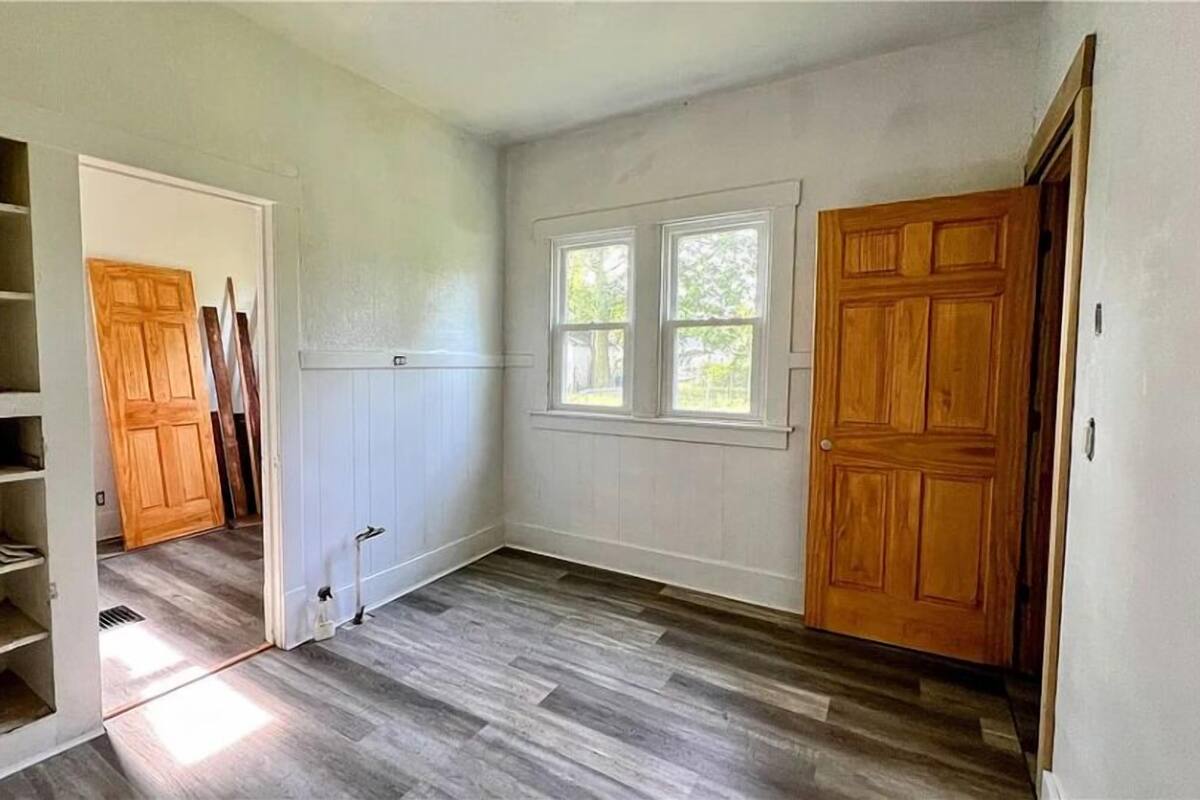 A room with a wooden floor, white walls, a window, and a door.