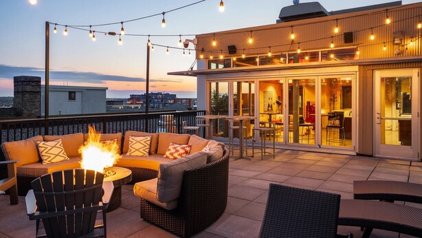 A rooftop terrace with outdoor seating, a fire feature, and string lights.