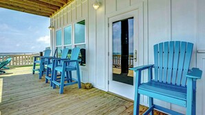 A covered deck with blue Adirondack chairs, a wooden floor, and a white exterior wall. - The Lazy Turtle, Beachfront (Crystal Beach)