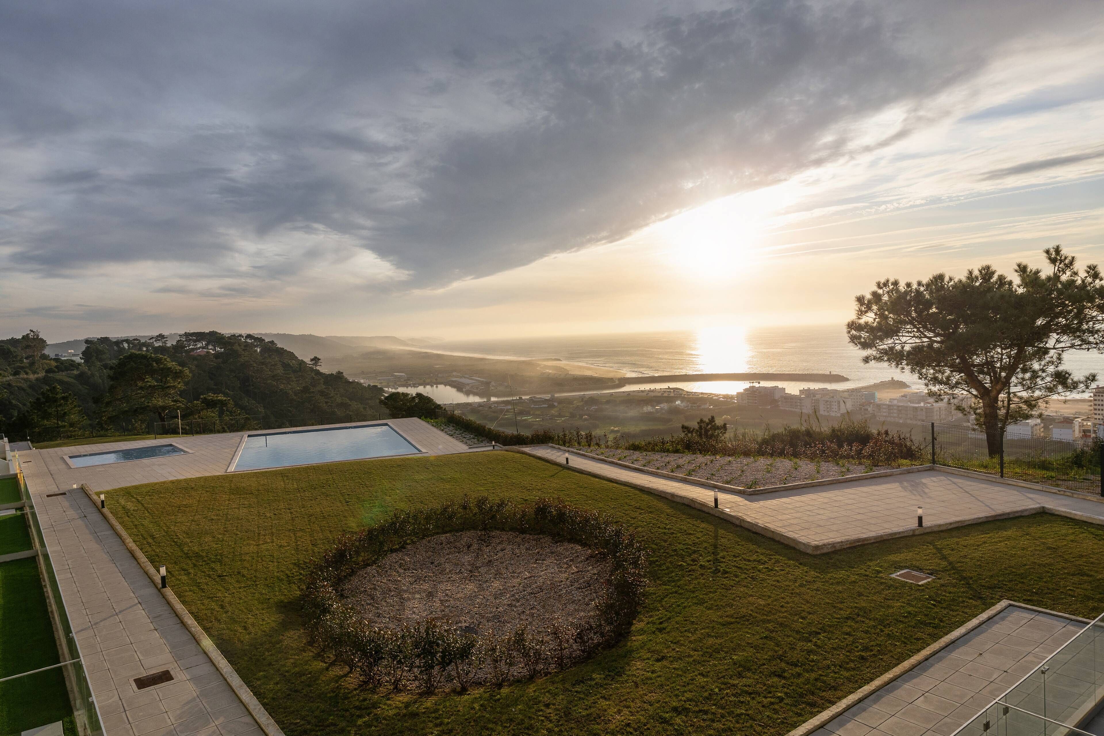 Une terrasse sur le toit avec une piscine, un jardin circulaire et une vue sur le coucher de soleil sur l’eau.