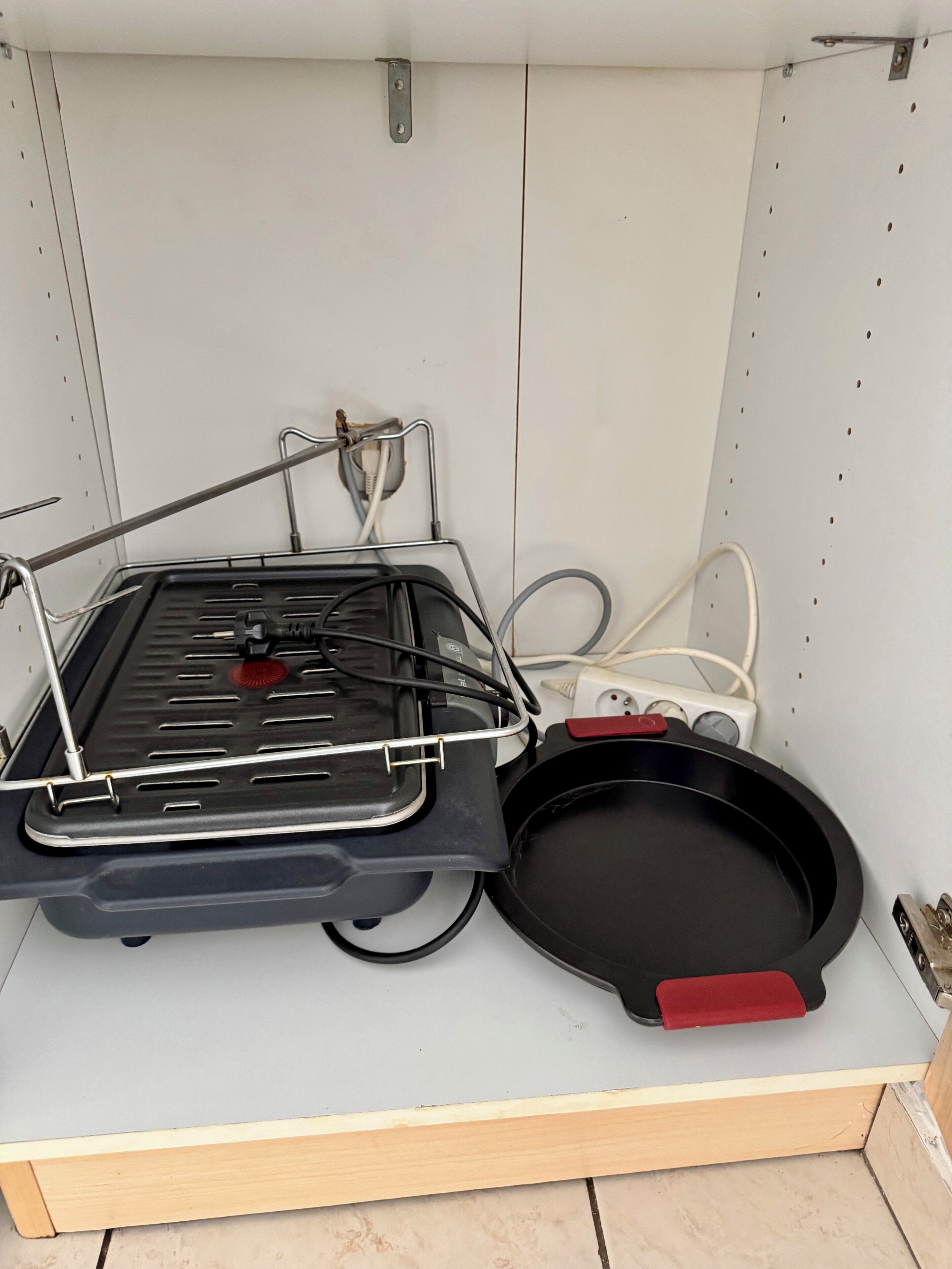 A compact kitchenette with a portable gas stove, a frying pan, and a power strip.