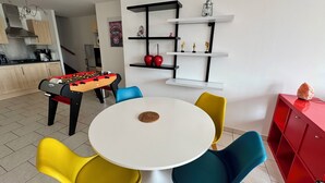 A modern living room with a round white table, colorful chairs, a foosball table, and a kitchen area with cabinets and a stove. - La Terrasse vue étangs, Table soccer, board games by BookingFuté (Socourt)