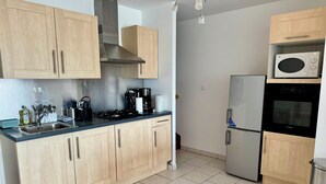 A modern kitchen with wooden cabinets, stainless steel appliances, and a tiled floor. - La Terrasse vue étangs, Table soccer, board games by BookingFuté (Socourt)