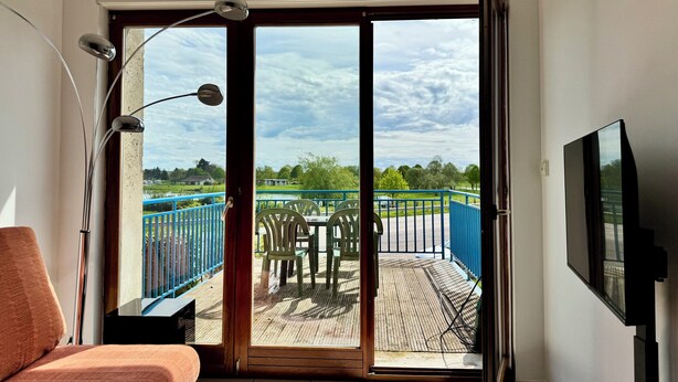 A room with a bed, a TV, and a sliding glass door leading to an outdoor deck with a table and chairs. - La Terrasse vue étangs, Table soccer, board games by BookingFuté (Socourt)