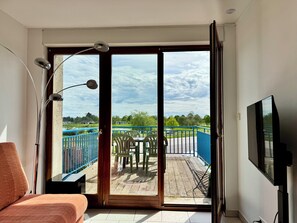 A room with a bed, a TV, and a sliding glass door leading to an outdoor deck with a table and chairs. - La Terrasse vue étangs, Table soccer, board games by BookingFuté (Socourt)