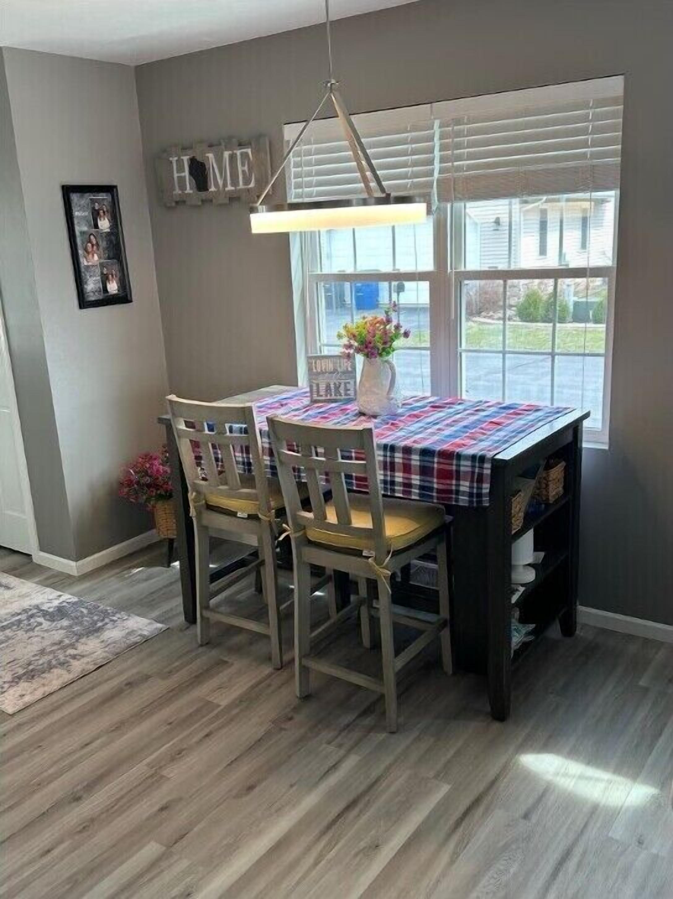 A dining area with a table set for four, a hanging light fixture, and a window with blinds.