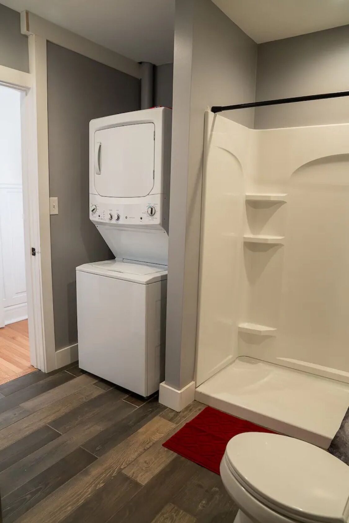A compact bathroom with a white toilet, a shower enclosure, and a stacked washer and dryer.