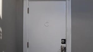 A closed door with a keyhole and a lock, a small circular emblem above the door, and a carpeted floor.