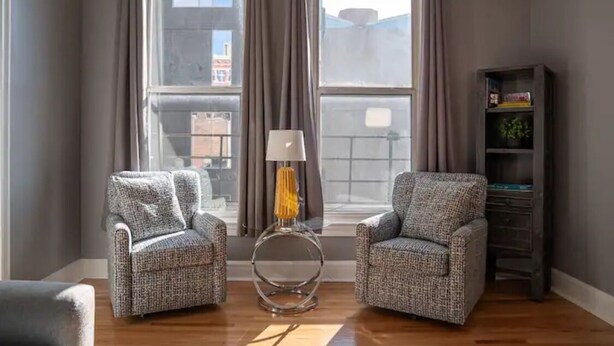 A living room with two patterned armchairs, a floor lamp, and a bookshelf.