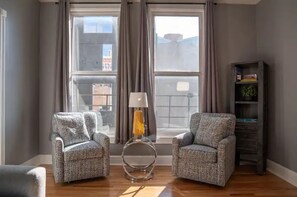 Una sala de estar con dos sillones estampados, una lámpara de pie y una estantería.