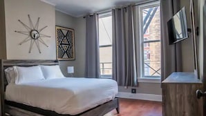 A bedroom with a wooden bed, a star-shaped wall decoration, a geometric wall art, a TV mounted on the wall, and a window with curtains.