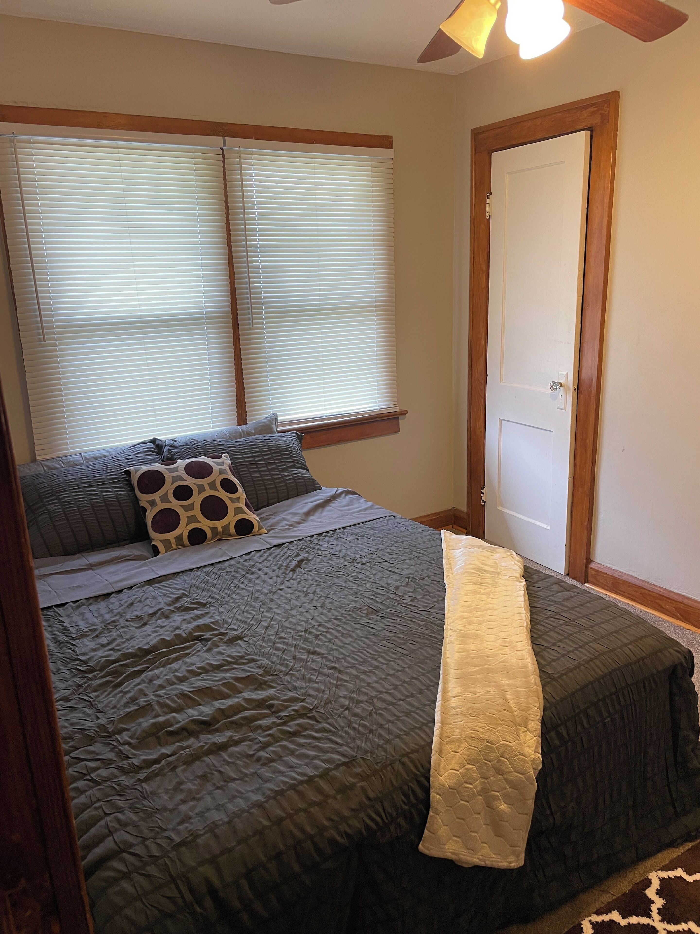 A bedroom with a bed, two windows with blinds, a door, and a ceiling fan.